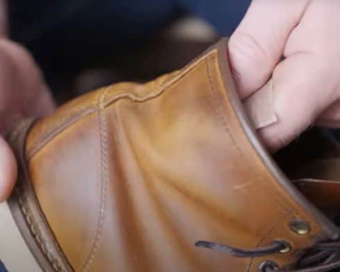 Man using 320 grit sandpaper to scuff up inside of leather boot so heel doesn't' slip.